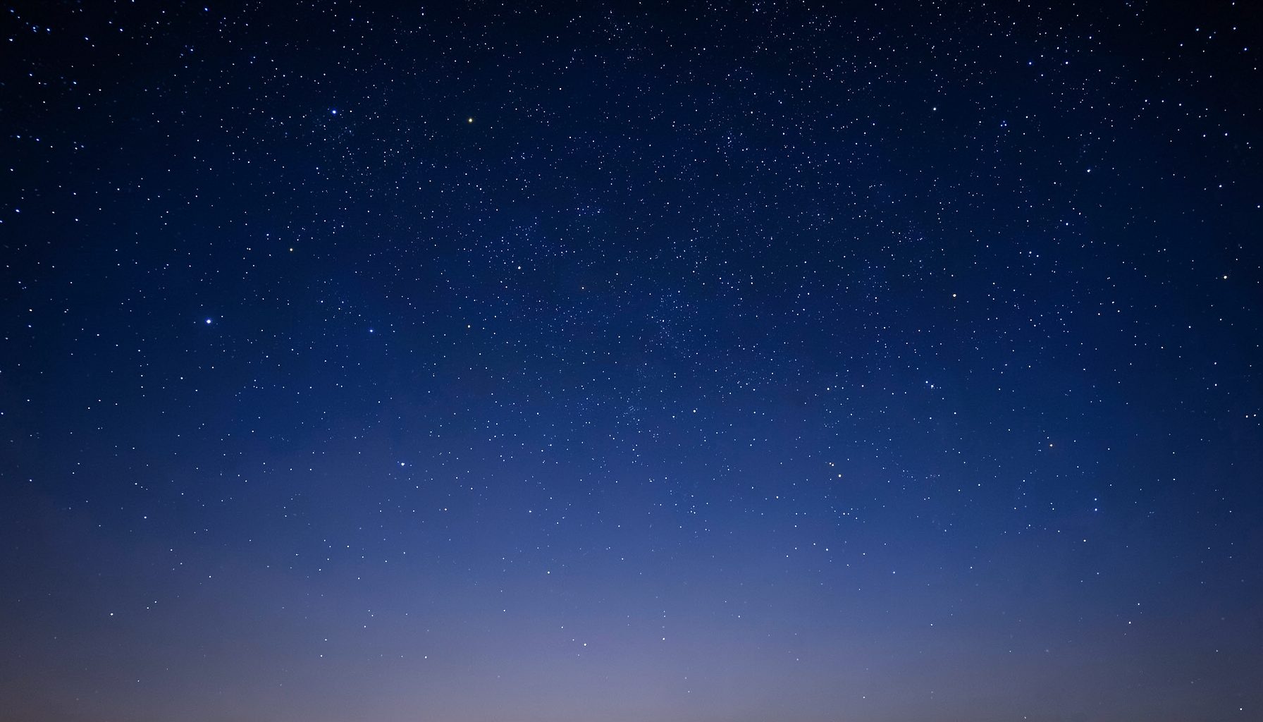 A calm night sky scattered with stars, deep navy blue fading into soft indigo at the horizon, evoking wonder and the human search for meaning
